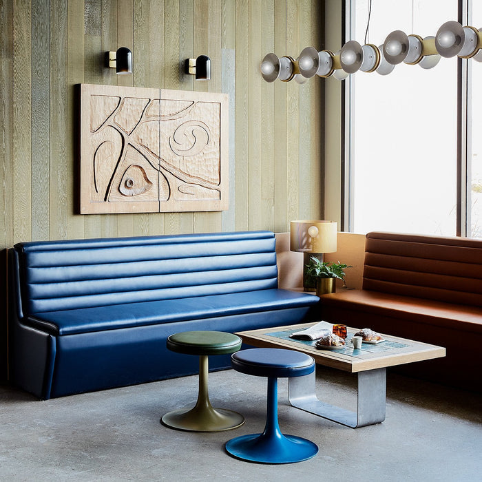 Two black wall sconces with brass backplates mounted above carved wood artwork in a cozy lounge with blue and brown banquette seating