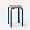Three-quarter view of Forma Stool showing round white oak top with exposed plywood edge and indigo powder-coated steel legs on light gray background