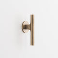 Front view of the natural brass Galley Pull showcasing its asymmetrical curved design and round backplate on a white background