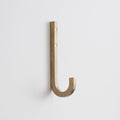 Angled view of J Hook in natural brass showing square solid-brass profile and two visible mounting screws on white wall