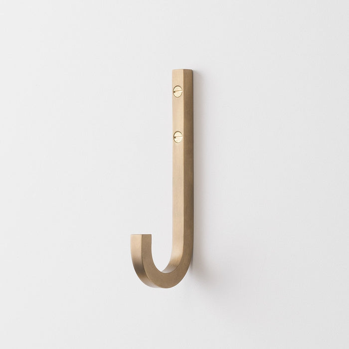Front view of J Hook in natural brass showcasing solid brass finish, visible mounting screws, and curved J shape on a white wall