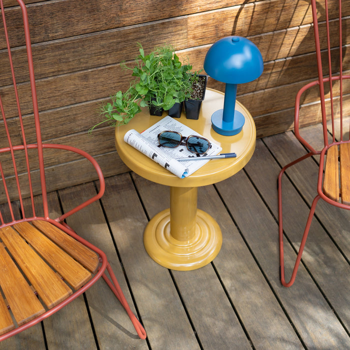Top view of Owen Side Table showing mustard yellow gloss pedestal, blue lamp and potted seedlings on a wooden deck