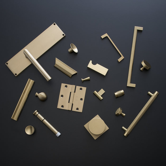 Overhead view of the Rhone Cast Brass Knob among assorted solid brass hardware on a dark background