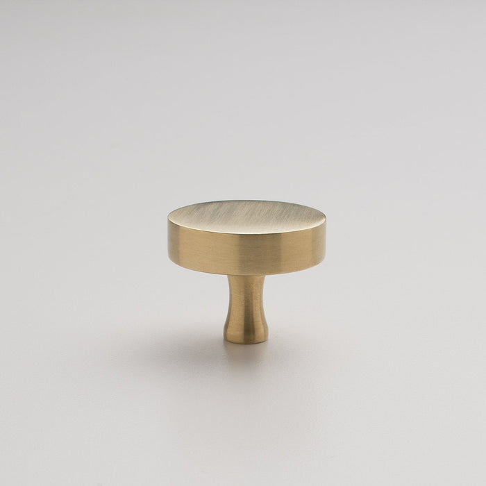 Front view of the natural brass Riverwood Knob showcasing its flat finish and fluted neck on a light background
