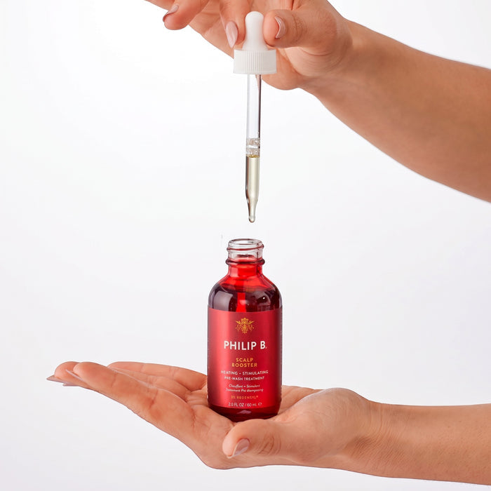 Shop Rescue Spa Scalp Booster pre-wash treatment in a red glass bottle with a dropper held over a hand.