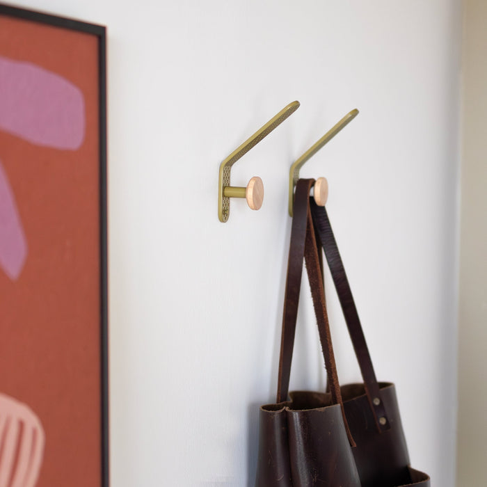 Tula hooks holding tote bags on a white wall beside framed artwork