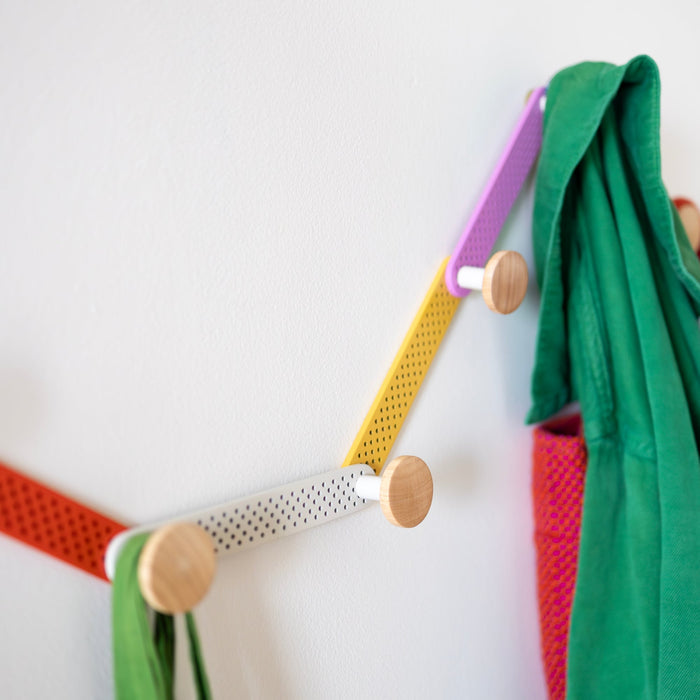 Angled view of the multicolor Tula Hook showcasing perforated metal and wood finials on a white wall
